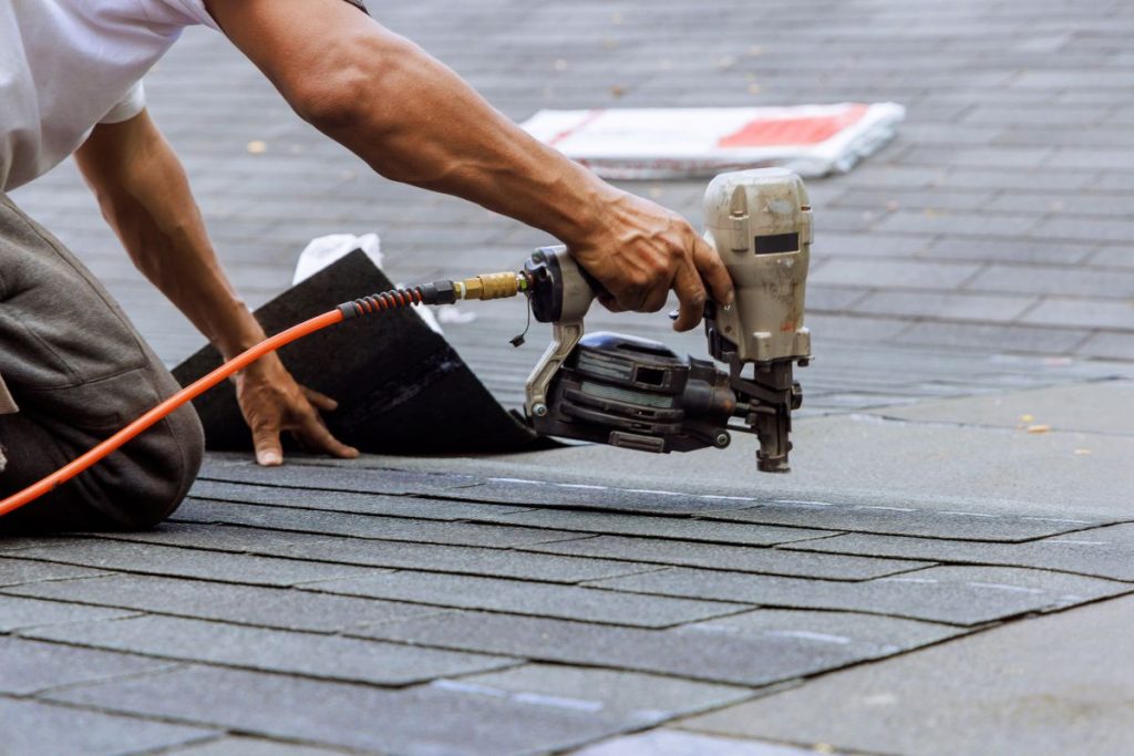 Air pneumatic nail gun used by roofer to install new asphalt bitumen shingles, Shoreview